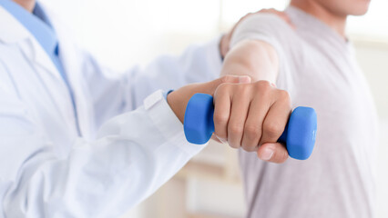 Doctor or Physiotherapist helping man exercise with dumbbell and physical therapy help for muscle or arthritis exercise in consulting exam. Doing the Rehabilitation therapy pain in clinic.