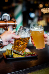 Two friends hands clinking glasses of craft beer at the pub or bar