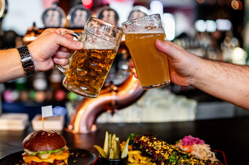 Two friends hands clinking glasses of craft beer at the pub or bar