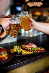 Two friends hands clinking glasses of craft beer at the pub or bar