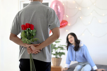 Man hiding beautiful red rose bouquet behind back, ready to give Valentine flower present to lover girlfriend for celebration, couple make surprise, love and happiness. Happy Saint Valentine Day.