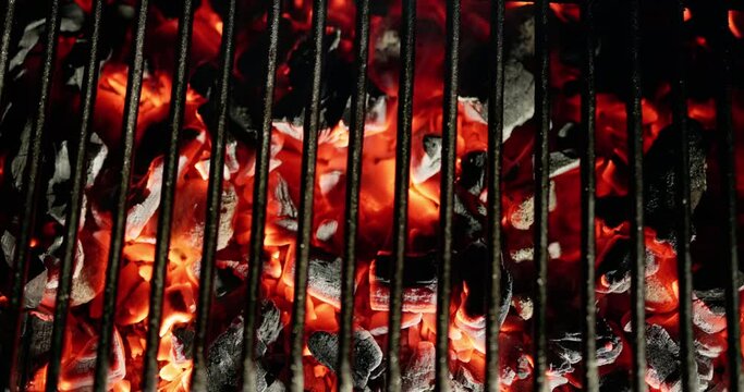 Close-up. Grill radiates inviting warmth, fueled by burning coals that promise mouth watering barbecue. Red hot coals crackle under grill grate, setting stage for fun outdoor feast. AD. Copy space.