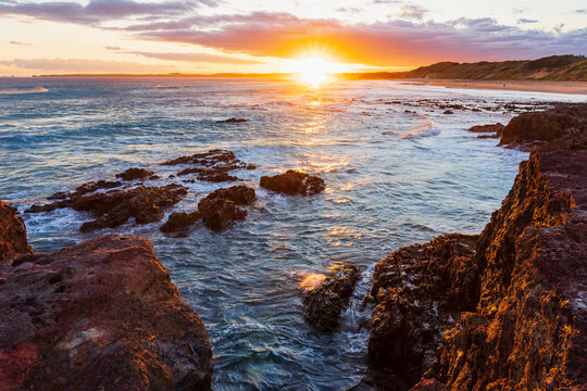 Bright sunset over a rocky coastline with gentle waves