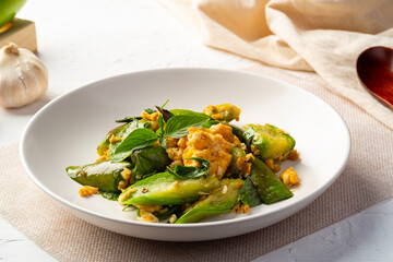 Stir fried Long Green Eggplant with Eggs and Sweet Basil leaf in white plate.