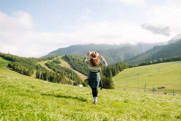 Woman walking on through green grass valley on background big mountains. Hiker resting. Beautiful National park. Fashion, beauty, tourism, resting concept.