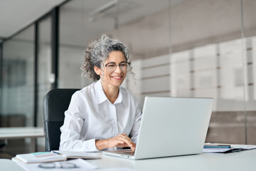 Smiling mature business woman executive working in office using laptop. Happy professional senior...