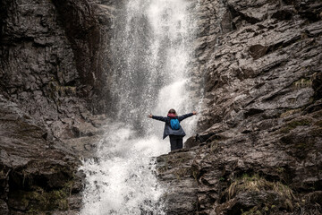 Obraz premium A girl and a dog stand against the backdrop of a waterfall. Beautiful nature. Splashes of water. American Staffordshire Terrier. Mountains.