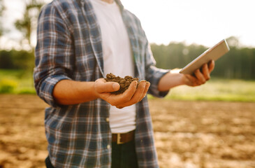 Farm hand holds black soil in her hands and checking with a digital tablet. Concept of agriculture,...