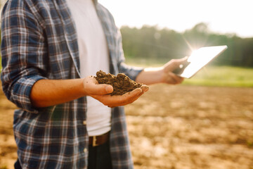 Farm hand holds black soil in her hands and checking with a digital tablet. Concept of agriculture, technology, business and ecology.