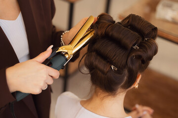 Portrait happy woman hairdresser stylist skillfully curling hair with golden iron in salon,...