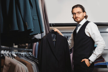 Portrait business gentleman in glasses chooses to buy suit jacket in shop store classic clothes for men