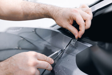 Master tucks edge of protective vinyl film behind of car part. Transparent protection with from gravel chips and scratches