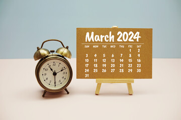 March 2024 monthly calendar on easel stand with alarm clock on pastel background