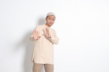 Portrait of unpleasant Asian muslim man in koko shirt with skullcap forming a hand gesture to avoid...