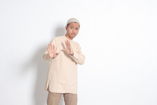 Portrait of unpleasant Asian muslim man in koko shirt with skullcap forming a hand gesture to avoid something or bad things. Isolated image on white background