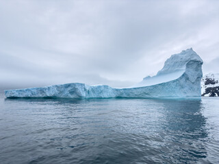 A huge high breakaway glacier drifts in the southern ocean off the coast of Antarctica at sunset, the Antarctic Peninsula, the Southern Arctic Circle, azure water, cloudy weather