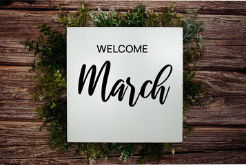 Welcome March text message with green leaf decoration on wooden background - obrazy, fototapety, plakaty