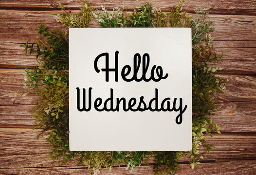 Hello Wednesday text message with green leaves decoration on wooden background