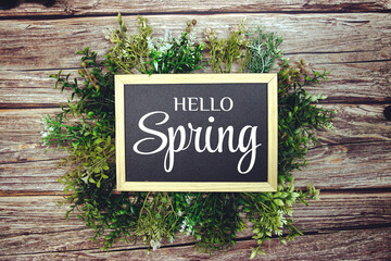 Hello Spring text message with green leaves decoration on wooden background