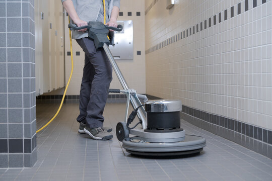 unrecognizable woman cleaning a washhroom floor with a buffer machine