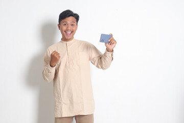Portrait of excited Asian muslim man in koko shirt holding mobile phone and playing games on his...