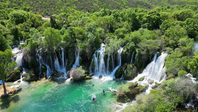 Aerial view of Kravica Waterfall in Bosnia and Herzegovina. People enjoying themselves on the boats next to the waterfall. Unique natural beauty in the Trebizat River for holidays and leisure time.