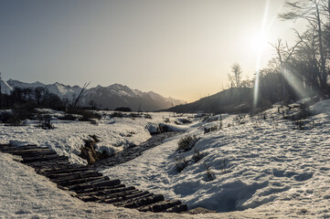 Snow covered bridge with Andes mountains in the background at golden hour. Ushuaia Emerald Lagoon