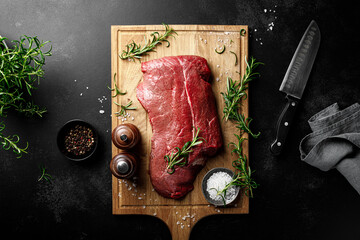 Beef meat entrecote on a cutting board, raw beef meat fillet on black background, top view
