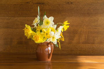 Happy easter holidays concept; Beautiful bouquet of yellow jonquil or daffodils in vase on a wooden background on sunlight