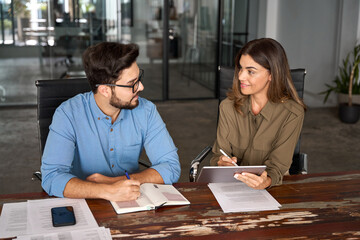 Two happy busy business people talking using digital tablet in office. Smiling professional...