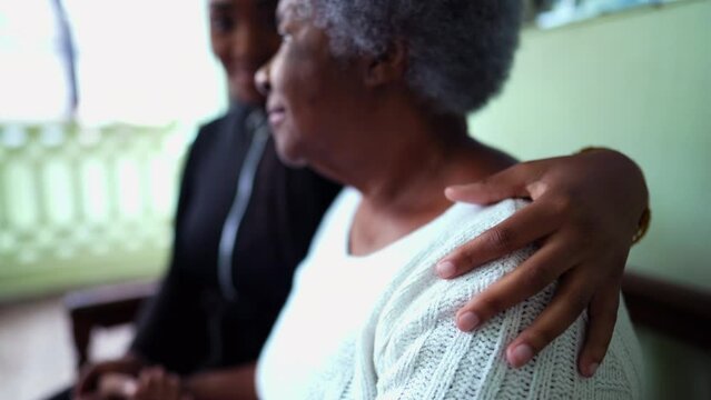 African American granddaughter caring for elderly grandmother in old age with arm around shoulder showing help and support for senior woman in 80s, inter-generational family care