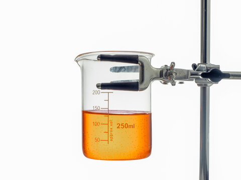 close up of a vintage borosilcate laboratory glass beaker and retort lab stand with amber liquid for analysis testing isolated on a white background