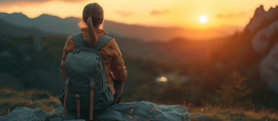 Back view young woman wearing a backpack and sit on stone in mountain at sunset. AI generated image - obrazy, fototapety, plakaty