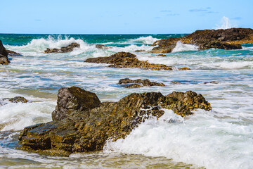 Australian coast with volcanic rocks at the shore, view from the beach to the horizon with blue water with waves on a summer sunny day.