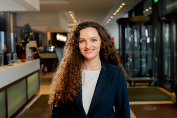 smiling curly female employee stands in the hotel lobby staff manager or receptionist hospitality