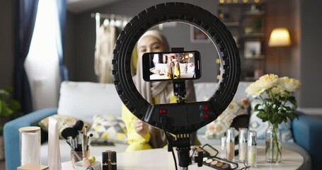 Female beauty blogger recording video. Display screen of smartphone shooting video, circular ring lamp. Beauty secrets and life hacks, woman shares experience on camera, shows cosmetic products.