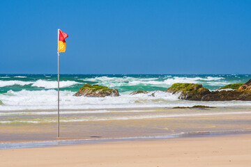 Red and yellow flag of lifeguards on the beach, rough ocean with high waves, seaside landscape on a...