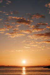 silhouette of the coast against the backdrop of the setting sun and clouds in the sky, the sun's path is reflected on the sea water