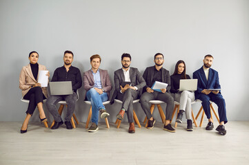Young professional business people sitting on the chairs in row and looking at the camera. Group of...