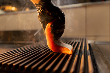 close-up of a chef's hand in a glove puts a raw piece of salmon on the grill in a restaurant kitchen