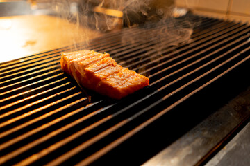 close-up of appetizing juicy raw piece of salmon fish grilled with smoke in restaurant kitchen