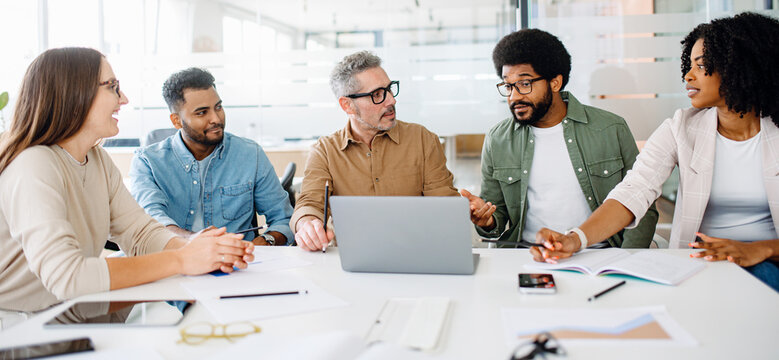 A lively discussion unfolds among four colleagues around a table, with bright smiles indicating a warm and collaborative brainstorming session in a well-lit office.