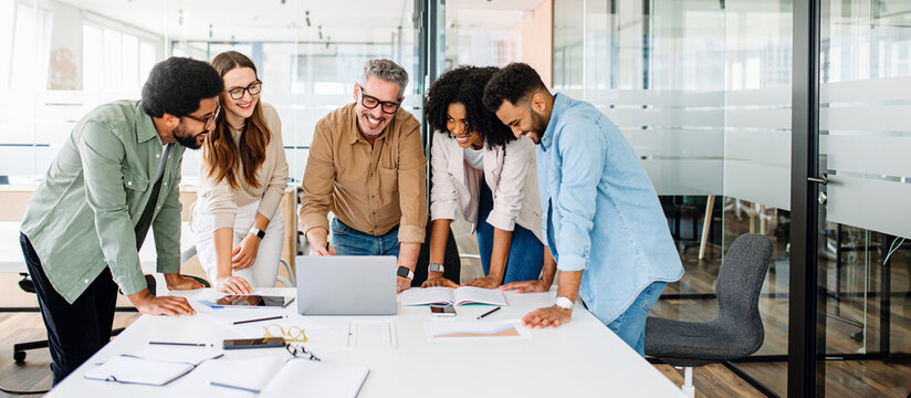 A panoramic view of a motivated team intensely focused on a computer screen, capturing the essence of a strategic work session in a contemporary, light-filled office. Diverse work group brainstorming
