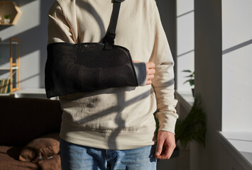 Close-up photo of a man's arm in a plaster cast standing in the living room at home or in hospital...