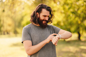 Outdoors portrait of a bearded man with long hair checking his smart watch.