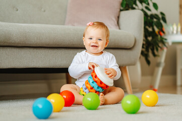 Cheerful baby girl is sitting on the floor while playing with her toys.