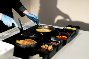 close-up buffet line open kitchen and hotel chef puts fried eggs and omelette on a plate for...