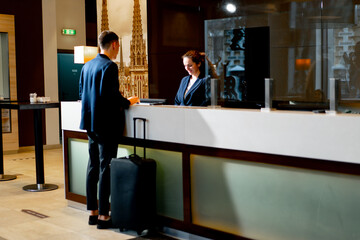 The receptionist at the counter meets the guest with luggage in the hotel business travel hospitality