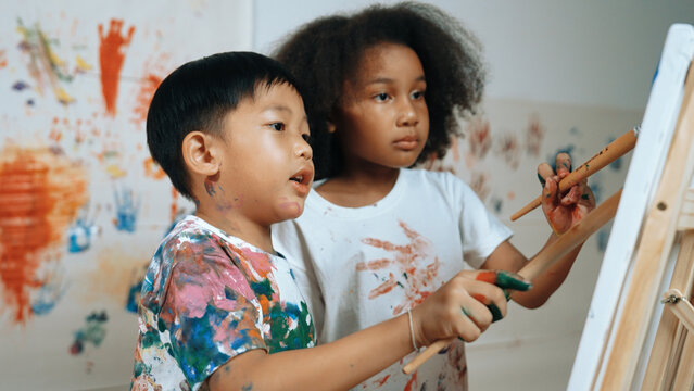 Happy creative african girl painted or draw canvas together with asian boy. Group of playful student create funny painting or artwork painted by watercolor. Creativity activity concept. Erudition.