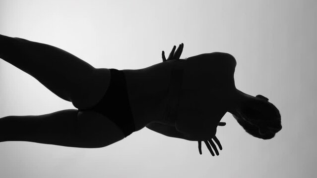 Captured in vertical format, a woman's silhouette is dramatically encased in monochrome light, her costume molding to her body in a display of elegance and strength. High quality 4k footage